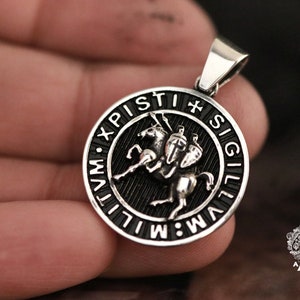 May include: A silver pendant with a black enamel design of a knight on horseback. The pendant is inscribed with the words "XPI. PISTI. SIGILLVM."