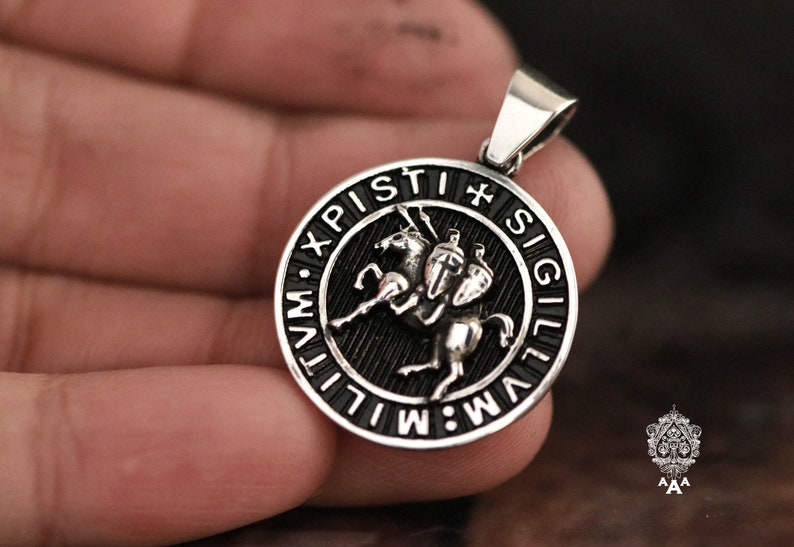May include: A silver pendant with a black enamel design of a knight on horseback. The pendant is inscribed with the words "XPI. PISTI. SIGILLVM."