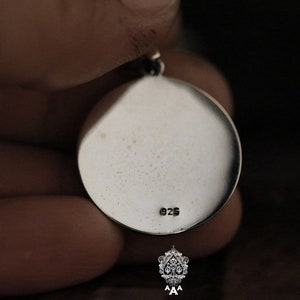 May include: Silver pendant with a round shape and a smooth surface. The back of the pendant has the number "925" stamped on it.