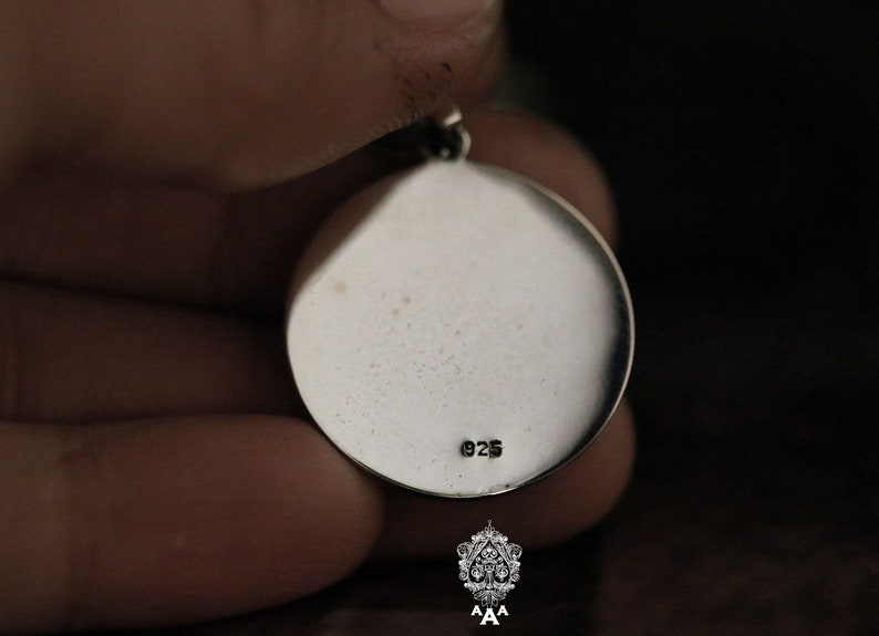 May include: Silver pendant with a round shape and a smooth surface. The back of the pendant has the number "925" stamped on it.