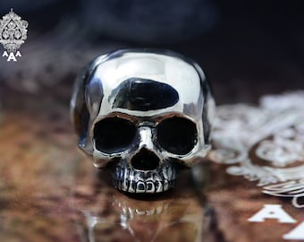 May include: A silver skull ring with a highly polished finish. The skull is detailed with eye sockets, a nose, and a mouth with teeth.