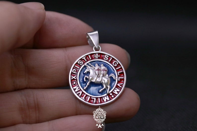 May include: Silver pendant with a blue and red enamel design. The pendant features a knight riding a white horse with a red cross on its chest. The inscription around the edge reads "NOX PISTI SIGILLVM".