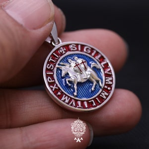 May include: A silver pendant with a red, white, and blue enamel design. The pendant features a knight riding a horse with a cross on his shield. The text around the edge reads "SIGILLVM MILITVM XPI STV", which is Latin for "Seal of the Knights of Christ".