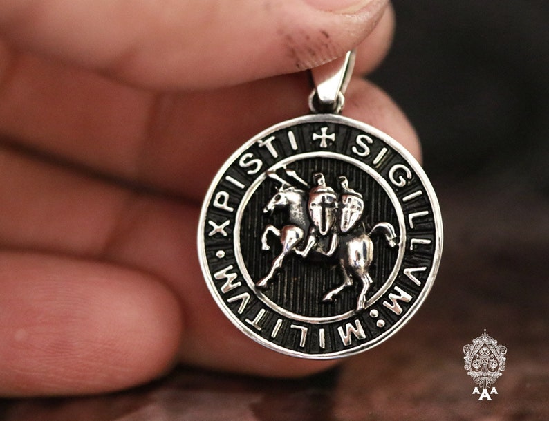 May include: Silver pendant with a black enamel design of a knight riding a horse. The pendant is surrounded by a circular inscription that reads "SIGILLVM XPISTI", which is Latin for "Seal of Christ".