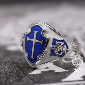 以下が含まれることがあります： 青と白のエナメルデザインのシルバーリング。リングには十字架の盾と、馬に乗った騎士の小さな盾が描かれています。