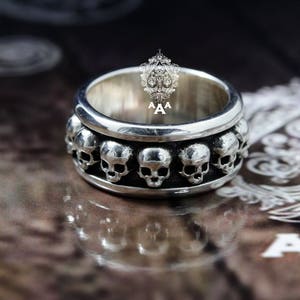 May include: A silver ring featuring a row of skull designs around the band.