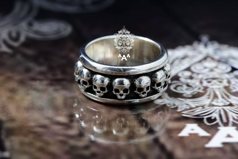 May include: A silver ring featuring a row of skull designs around the band.