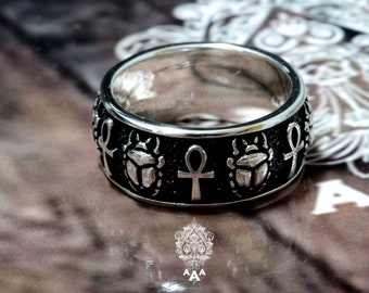 May include: A silver ring with a black band featuring an Egyptian ankh symbol and scarab beetles.