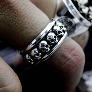 May include: A silver ring with a band of skulls that rotate around the finger.