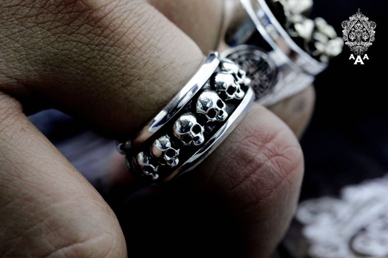 May include: A silver ring with a band of skulls that rotate around the finger.
