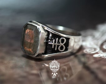 May include: A silver ring with a black stone and a silver symbol on the band. The symbol is a cross with a number 8 inside.