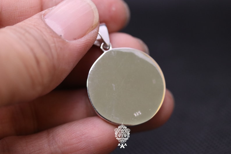 May include: Silver pendant with a round, smooth surface. The back of the pendant has the number 925 stamped on it.
