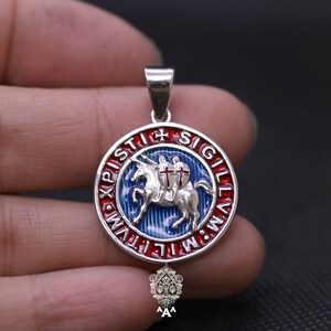 May include: Silver pendant with a blue, red, and white enamel design. The design features a knight riding a horse with a cross on its chest. The pendant is surrounded by a circle of text that reads "IN HOC SIGNO VINCES" in Latin.