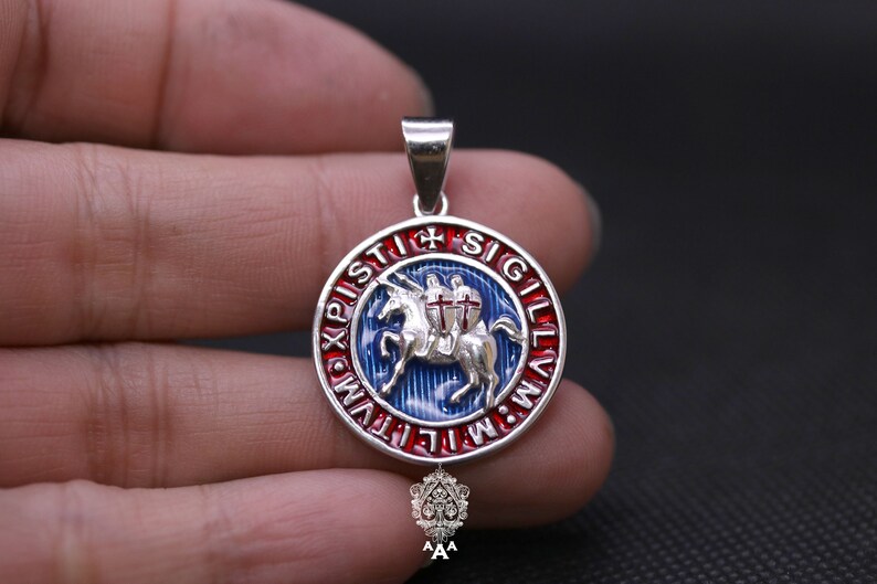 May include: Silver pendant with a blue, red, and white enamel design. The design features a knight riding a horse with a cross on its chest. The pendant is surrounded by a circle of text that reads "IN HOC SIGNO VINCES" in Latin.