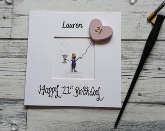 May include: A white card with a pink heart balloon with the number 21 on it. The card says "Lauren" and "Happy 21st Birthday".