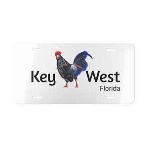 May include: White metal license plate with a black rooster illustration and the text "Key West Florida".