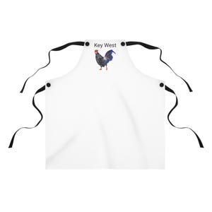 May include: White apron with adjustable straps and black buttons. The apron has a rooster graphic and the text "Key West" printed on the front.