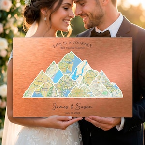 May include: A copper-colored metal sign featuring a mountain range design with map inserts. The sign includes the text "LIFE IS A JOURNEY Best Traveled Together", names "James & Susan", and the date "July 18, 2024". The sign is held by a couple.