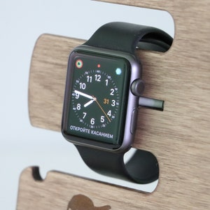 May include: A black Apple Watch with a black band on a wooden stand. The watch face displays the time, date, and the text "ОТКРОЙТЕ КАСАНИЕМ".