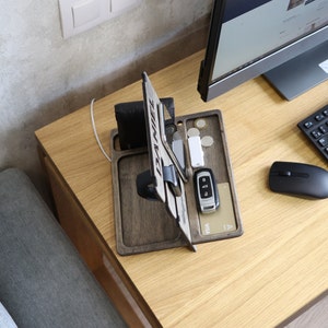 May include: Wooden desk organizer with a phone stand, watch holder, and slots for cards and keys. The organizer is on a light wood desk with a computer monitor, keyboard, and mouse.