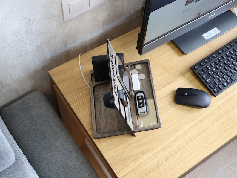May include: Wooden desk organizer with a phone stand, watch holder, and slots for cards and keys. The organizer is on a light wood desk with a computer monitor, keyboard, and mouse.