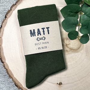 May include: Dark green socks with a brown label that says "MATT BEST MAN - 05.18.25 -" with a bow tie icon.
