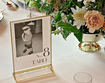 May include: Elegant table setting with white tablecloths, gold-rimmed plates, and floral centerpieces. Includes a menu card, table number 8, and tall candles in gold holders. The menu lists main course options.
