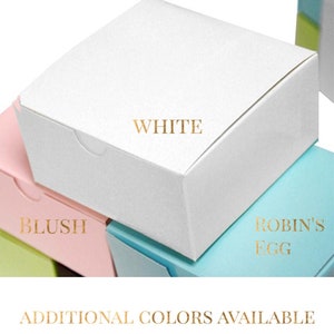 May include: Stack of square gift boxes in various colors, including white, blush pink, and robin's egg blue. The top box is white with the word "WHITE" printed in gold lettering.  Additional colors available.