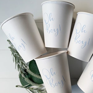 May include: Five white paper cups with blue lettering that says "Oh Boy!"  The cups are arranged in a circle on a white surface.