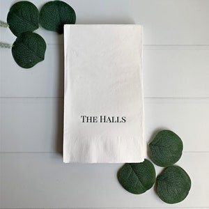 A photo of a beautifully set wedding table with elegant personalized dinner napkins. The napkins feature the bride and groom's first names or last name, printed in a stunning font and surrounded by a delicate decorative border.