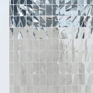May include: A white cake with colorful sprinkles and a cake topper that says "Mrs. Always" sits on a white pedestal. The background is a wall of reflective, square tiles in shades of silver and gray.
