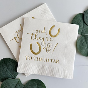 May include: White paper napkins with gold foil lettering that reads "...and they're off! To the altar" with two gold horseshoe symbols.