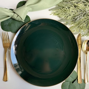 Puede incluir: Un plato de cena de color verde oscuro con un borde dorado, un tenedor dorado, un cuchillo dorado y una cuchara dorada. El plato est&aacute; rodeado de hojas verdes.
