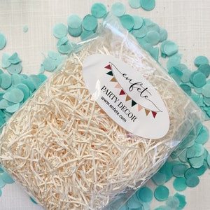 Op de afbeelding: Een doorzichtige plastic zak gevuld met versnipperd papier, met een ovaal wit etiket met de tekst "enfete PARTY DECOR www.enfete.com". Lichtblauwe confetti cirkels zijn verspreid.