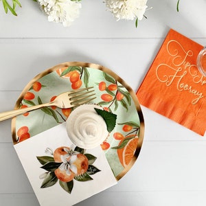 Op de afbeelding: Een feestelijke tafelsetting met een gouden vork, een cupcake en een bord met een sinaasappel- en bladerontwerp. Een oranje servet met de tekst "Hip Hip Hooray" en een glas met een gestreept rietje zijn ook aanwezig. Thema: feest.