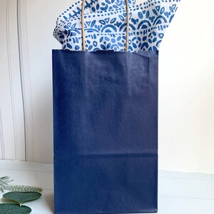 May include: A navy blue paper gift bag with white and blue patterned tissue paper peeking out of the top.