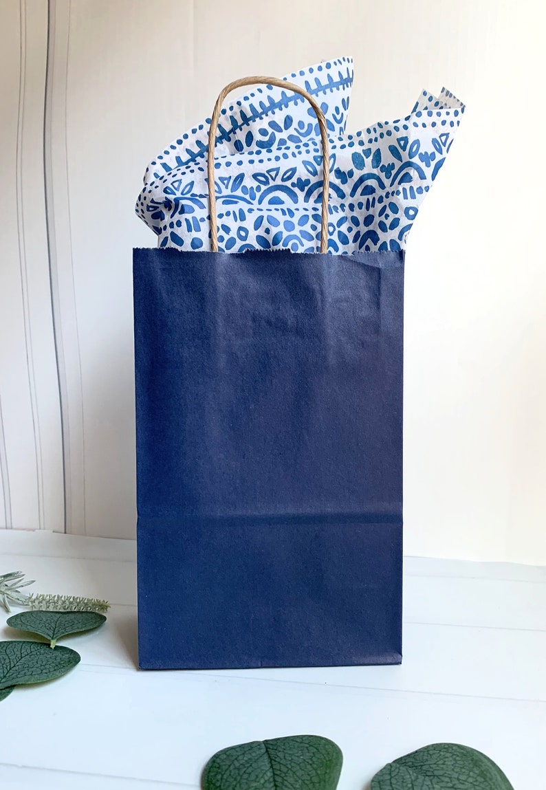 May include: A navy blue paper gift bag with white and blue patterned tissue paper peeking out of the top.