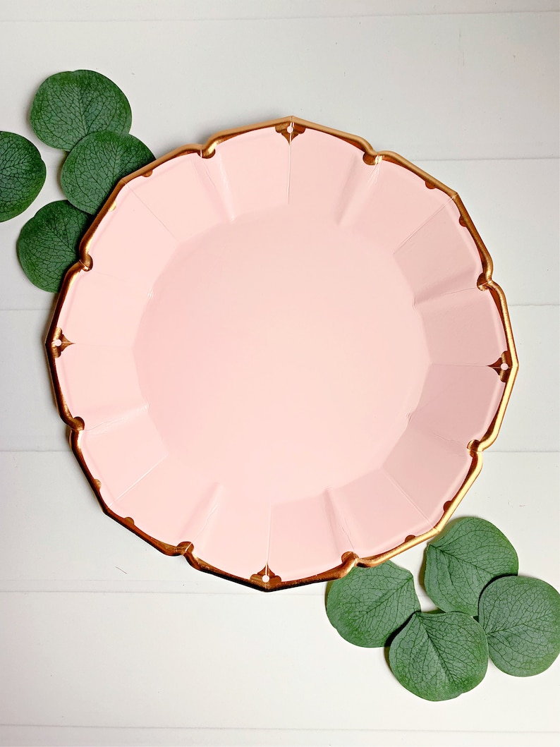 May include: Pink paper party plate with a gold rim. The plate has a scalloped edge and is perfect for a special occasion.