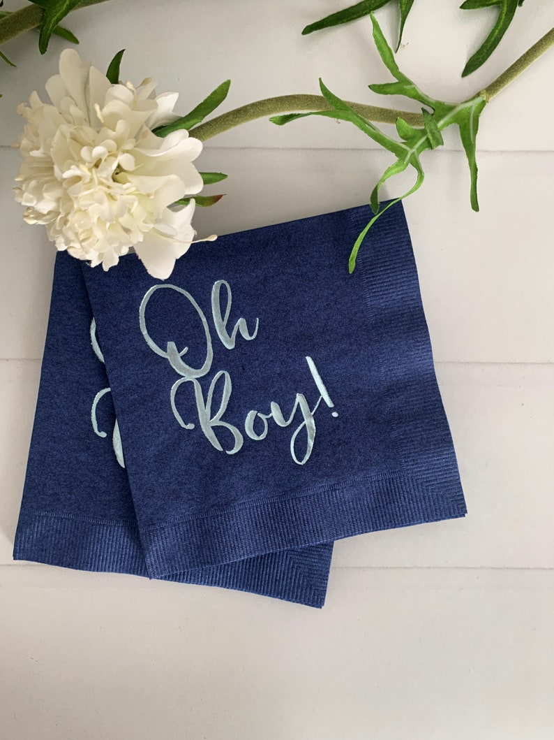 May include: Two navy blue paper napkins with white text that reads "Oh Boy!" in a light blue font.