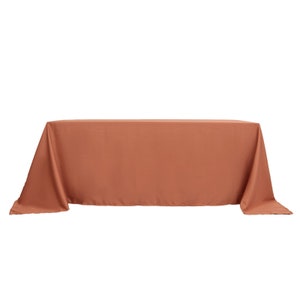 May include: A terracotta table cloth with a smooth, wrinkle-free finish. The tablecloth is laid out flat on a table.