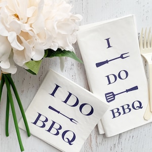 May include: Two white napkins with blue text and illustrations of grilling tools. The text on the napkins reads "I DO BBQ".