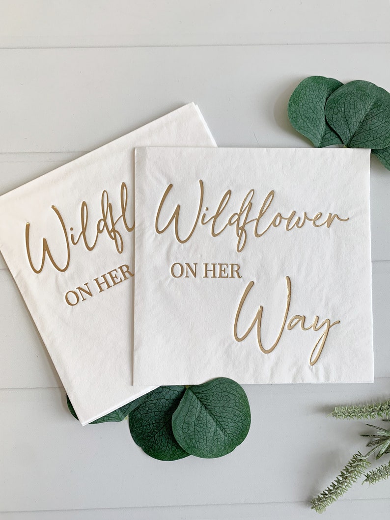 "Wildflower on her Way " in gold foil on white luncheon napkins - the perfect accent for your baby shower.  A fun baby shower theme for spring and summer babies. These gorgeous gold foiled "Wildflower on her Way " napkins are an EnFete original