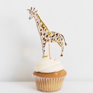 May include: A cupcake topped with white frosting and colorful sprinkles, decorated with a giraffe cupcake topper. The giraffe is illustrated in gold, purple, and blue.