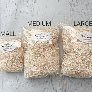 Op de afbeelding: Drie doorzichtige plastic zakken gevuld met beige cr&ecirc;pepapier, met de labels "SMALL", "MEDIUM" en "LARGE". Elke zak heeft een ovale sticker met de tekst "enfete PARTY DECOR" en een websiteadres. De achtergrond is een wit houten oppervlak.