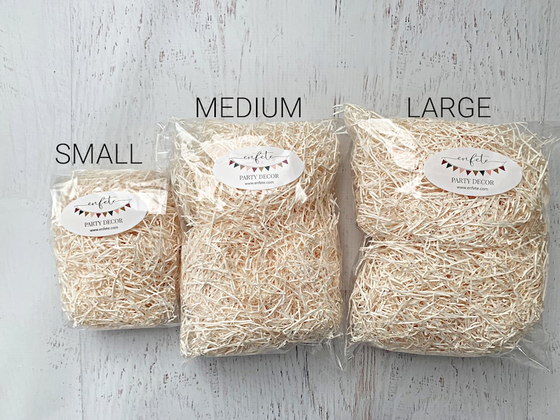 Op de afbeelding: Drie doorzichtige plastic zakken gevuld met beige cr&ecirc;pepapier, met de labels "SMALL", "MEDIUM" en "LARGE". Elke zak heeft een ovale sticker met de tekst "enfete PARTY DECOR" en een websiteadres. De achtergrond is een wit houten oppervlak.