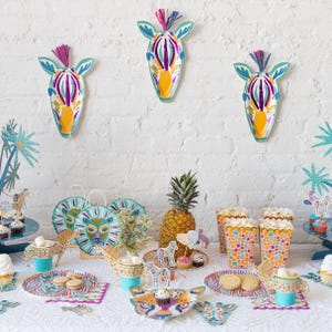 K&ouml;nnte beinhalten: Eine festliche Party-Tischdekoration mit Safari-Thema. Enth&auml;lt Zebra-Kopf-Wanddekoration, Teller, Tassen und Popcorn-Beh&auml;lter. Der Tisch ist mit einer Ananas, Cupcakes und Keksen dekoriert. Das Farbschema umfasst T&uuml;rkis, Gelb, Lila und Orange.