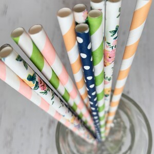 May include: A set of colorful paper straws with different patterns, including floral, polka dots, and stripes. The straws are in a clear glass.