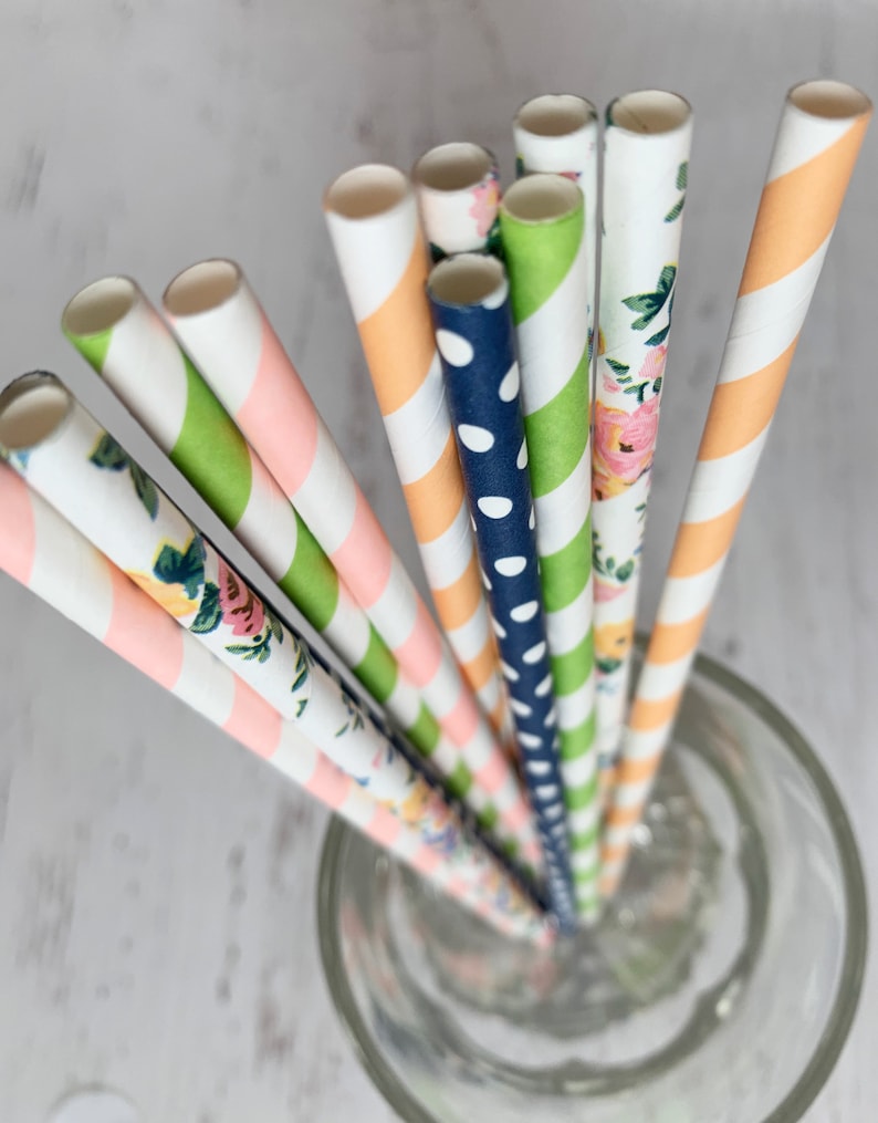 May include: A set of colorful paper straws with different patterns, including floral, polka dots, and stripes. The straws are in a clear glass.