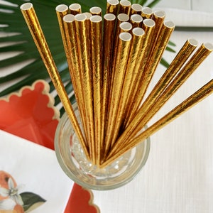 May include: A bunch of gold foil paper straws in a glass jar. The straws are arranged in a fan shape and have a textured surface.