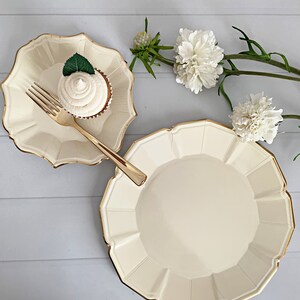 Op de afbeelding: Ivoor papieren borden met geschulpte randen en gouden rand. Een cupcake met witte glazuur en een muntblad ligt op een kleiner bord, met een gouden vork. Witte bloemen en groen op de achtergrond.
